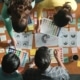 Illustration of graphic designers collaborating at a table, surrounded by laptops, sketchpads, and design tools, working together on creative projects.